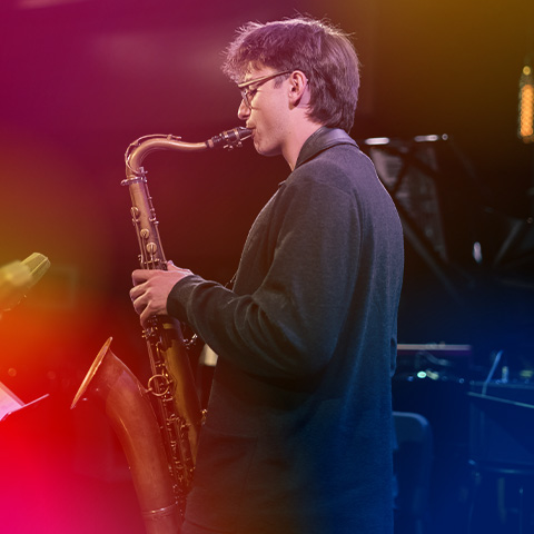 Jean Strauss from side angle playing the saxophone under stage lights