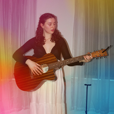 Photo of Vanessa Torre standing and playing the guitar