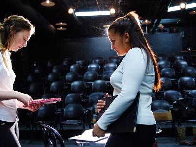 Two people discussing something on stage in front of empty audience seating