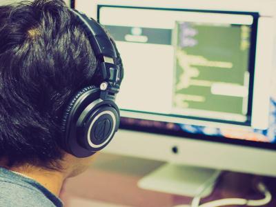 Young person wearing headphones facing multiple computer screens