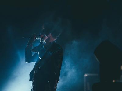 Vocalist singing into microphone on a dark and foggy stage