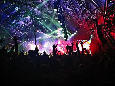 Silhouette of audience hands up at a concert with bright colorful stage lights.