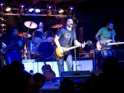 Three guitarists and a drummer on stage performing for a crowd