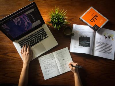 Aerial view of a desk with laptop, notebook, mug, books, and plant
