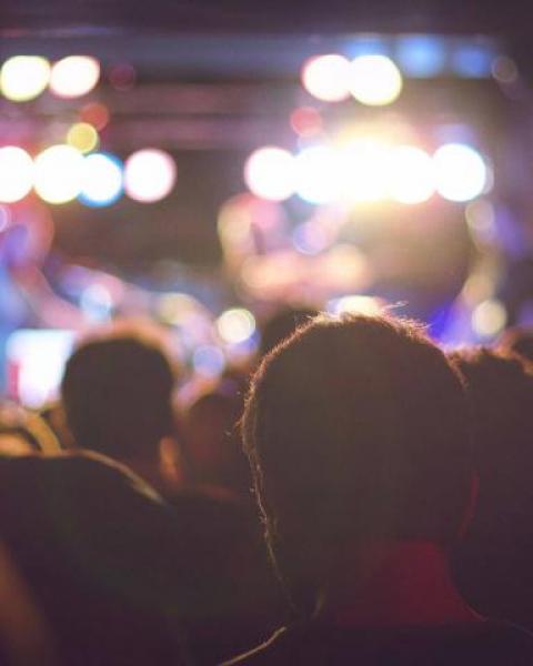 Crowd of people in a music venue bathed in bright colorful lights with musicians on stage