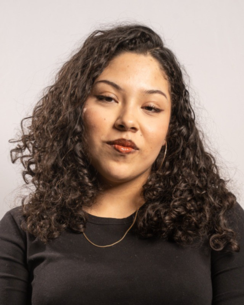 Student with olive skin and black curly hair smiles against a white background.
