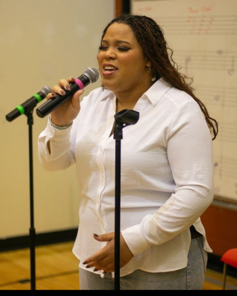Student sings into microphone at Stax Music Academy wearing a white dress shirt and golden braids.