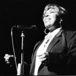 A black and white image of Roberta Flack standing at a mic taken from a low angle