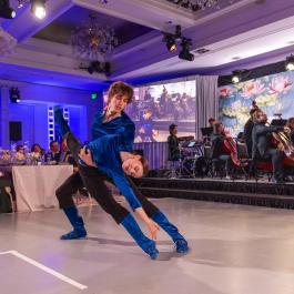 two dance students performing at the Soirée in black and black outfits. One student is holding the other's leg up to the sky.