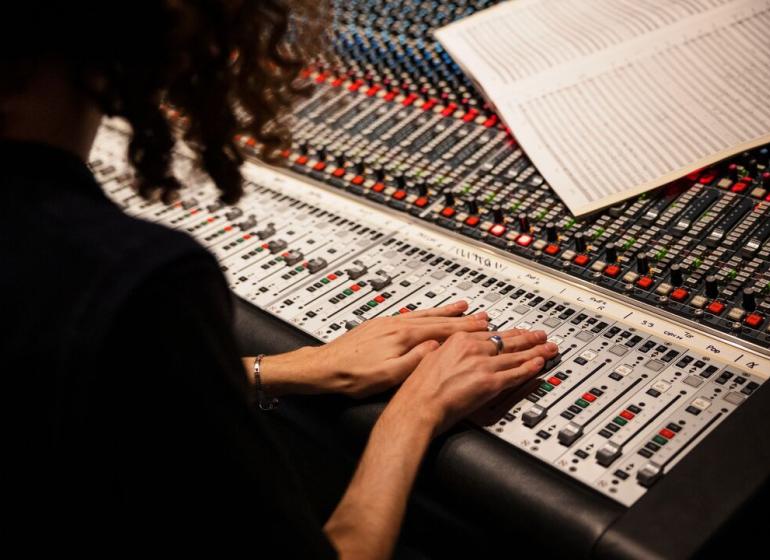 Producer adjusting levels on a soundboard and looking at sheet music