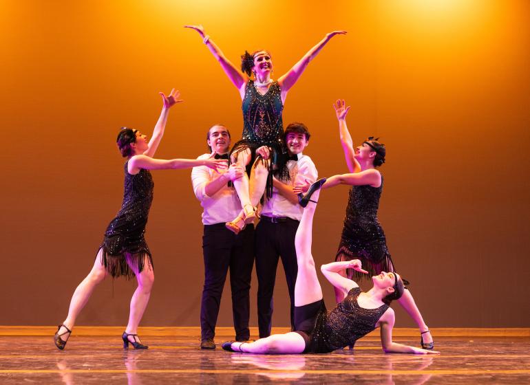 Maureen McMullan and student dancers in flapper outfits. McMullan is being held up in the air by two male dancers.