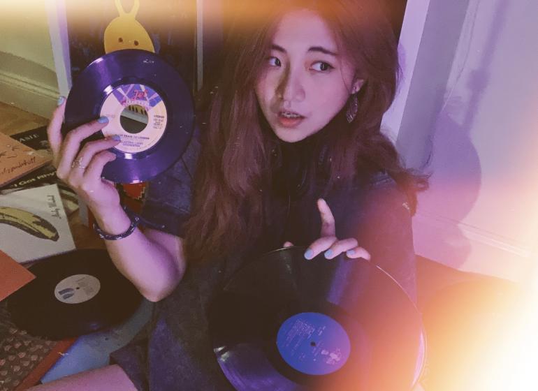 woman holding two vinyl records, surrounded by more records