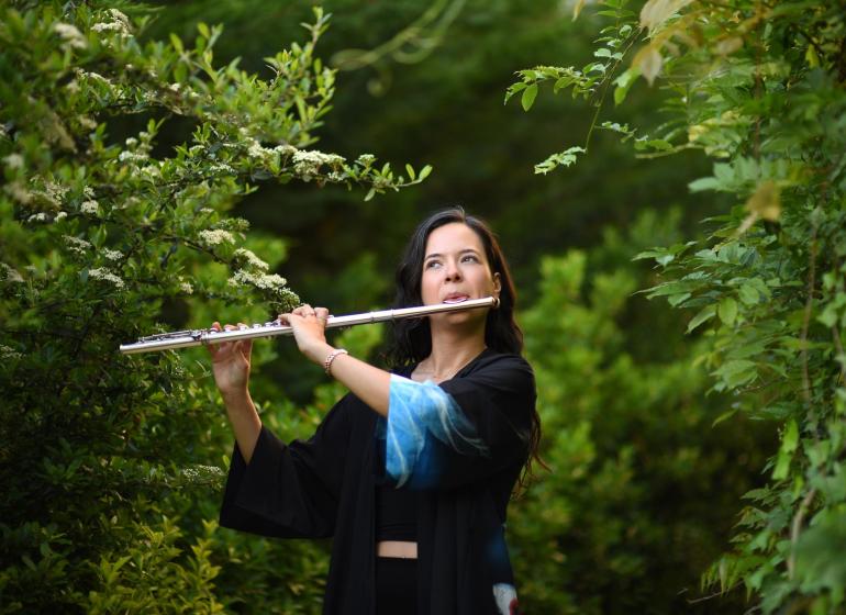 Yağmur Soydemir playing the flute outside among green trees