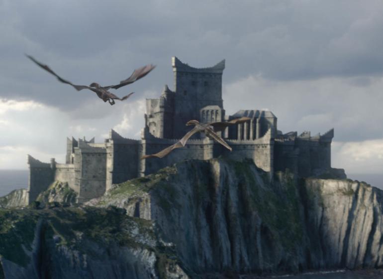 A scene from Game of Thrones season 8 where two dragons are flying in the foreground with Dragonstone in the background