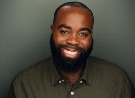 Ricardo Coke-Thomas headshot: smiling in a green/gray button down in front of an off-blue/gray wall.