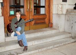 Mei Semones sits on steps with a guitar.