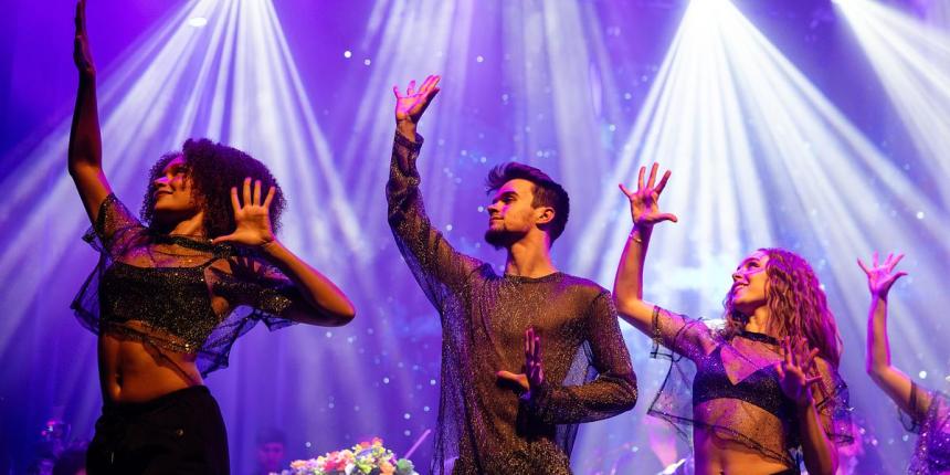 Students dancing on stage for the Coldplay Signature Series show with lots of spotlights in the background
