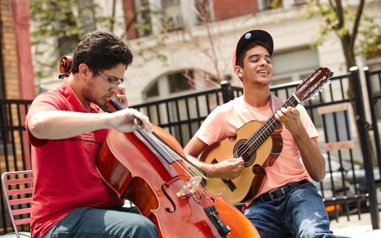 Two students playing cuatro and cello together outside