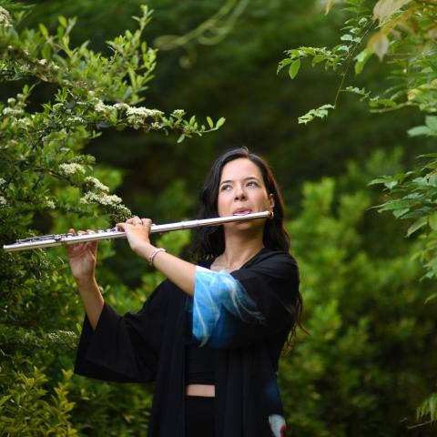 Yağmur Soydemir playing the flute outside among green trees
