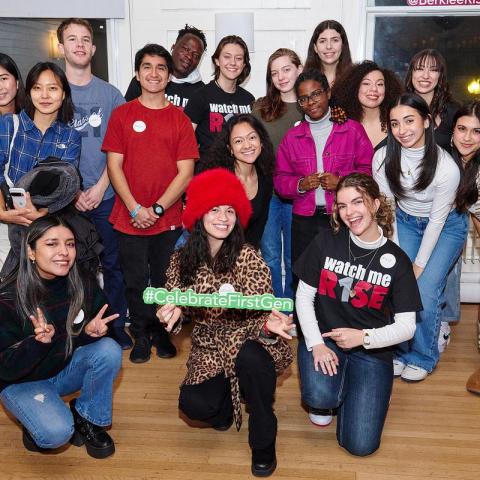 Group of students posing for a photo. Some kneeling, some standing straight. One student is a holding a sign that says "#Celebrate First Gen"