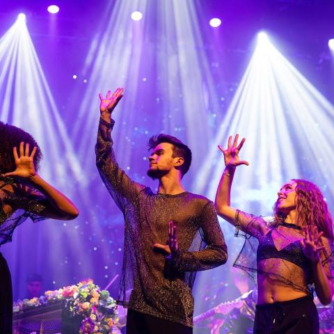 Students dancing on stage for the Coldplay Signature Series show with lots of spotlights in the background