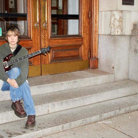 Mei Semones sits on steps with a guitar.