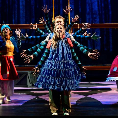 Theater students performing on stage in 'Alice by Heart' in a row with their arms spread out making a circle of arms