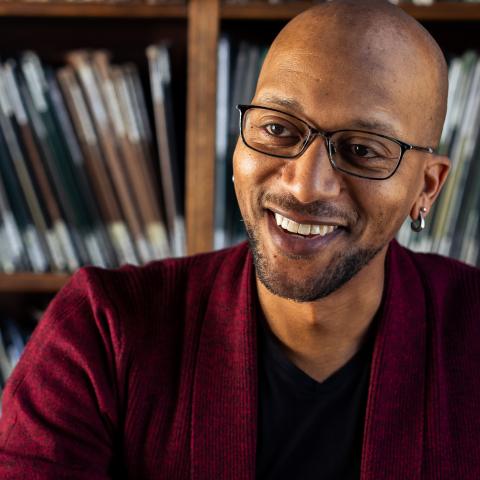 Headshot of Kevin Haden in a red suit with a black shirt in front of book shelves