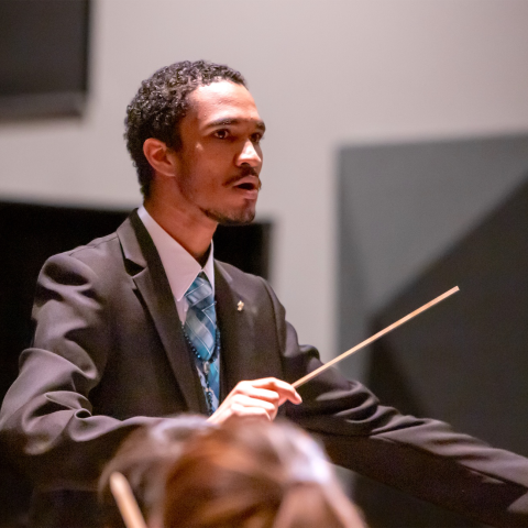 Conductor/percussionist Harold Rivas conducting an ensemble in a suit