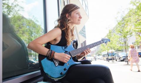 Woman playing guitar outside of 160 Massachusetts Avenue.