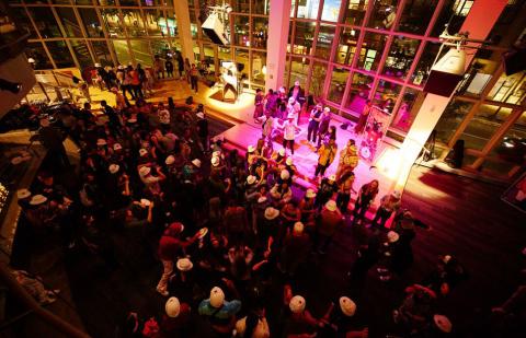 Berklee College of Music students perform in front of a caf show audience. The musicians are lit with pink lights