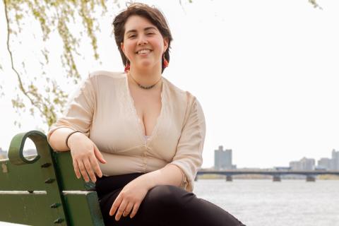 Gaby Pedraza sitting on a park bench with a body of water and a city skyline in the background