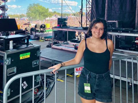 Nicol Kuburoglu stands backstage at an outdoor festival with a packed crowd in the background