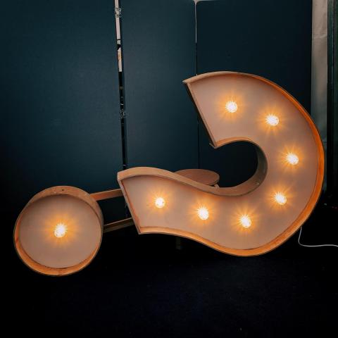 A metal sign in the shape of a question mark with lightbulbs on the inside