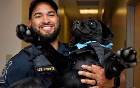 Sergeant Vicente smiles while holding Barklee the dog in his arms
