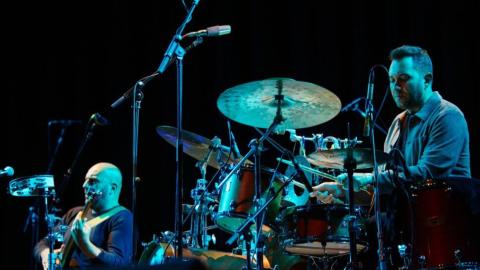 Photo of a drummer and guitarist performing on stage.