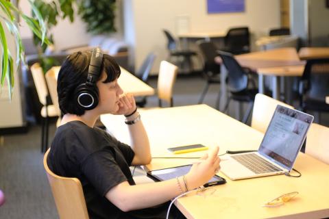 Student sits at a table wearing headphones and looking at computer