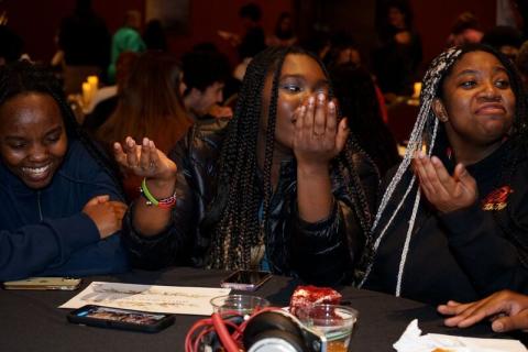 3 Black scholars initiative students sit next to eachother at a table smiling and laughing
