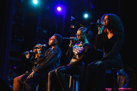 Four High School Academy vocalists sit on stools, each holding a microphone on the Berklee Performance Stage