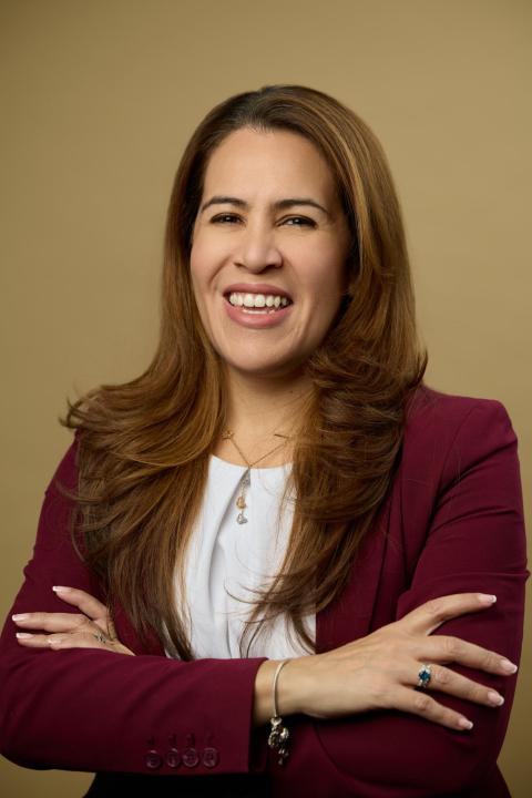 A woman smiles enthusiastically at camera while crossing her arms.