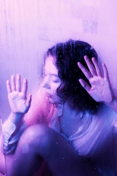 girl leaning up to glad or camera with both hands on the surface, monochromatic purple aura, head facing to the side, also leaning, glass is smudged. 