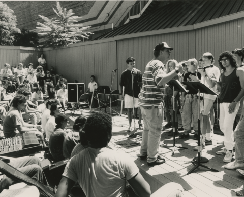 Student conducts other students singing, while more students sit in the audience during 1989 summer program