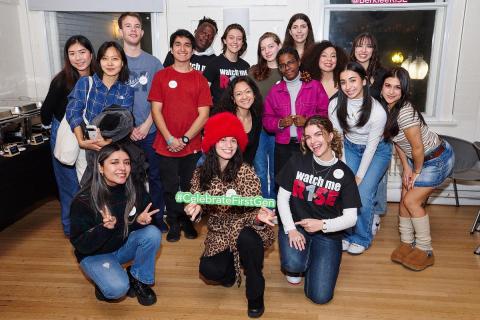 Group of students posing for a photo. Some kneeling, some standing straight. One student is a holding a sign that says "#Celebrate First Gen"