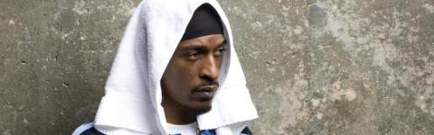 Headshot of Rakim standing against a concrete backdrop