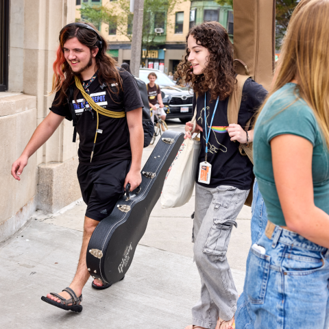 Two students walking down the street holding their instruments.