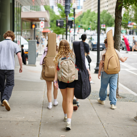 Students walking down the street with their guitars on their back.