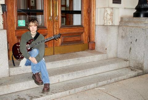 Mei Semones sits on steps with a guitar.