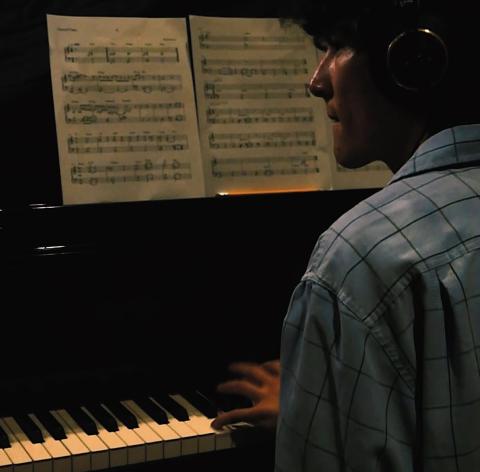 photo captured from over the shoulder of man sitting at piano looking at sheet music while playing 