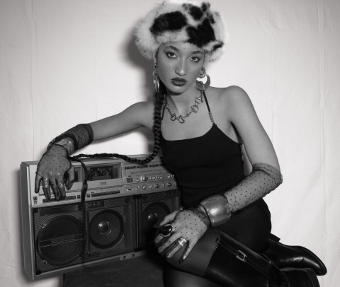 Black-and-white portrait of Jazz Cuti in a fur hat, gloves, and boots posing with a vintage boombox, styled with bold jewelry and a confident expression.