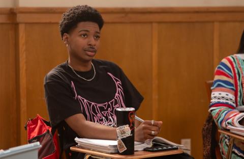 Jordan Aaron Hall as Amir sits at a desk in a college classroom